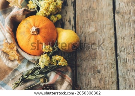 Stylish pumpkin, autumn leaves, flowers, pears and cozy blanket on rustic old wooden background. Rural fall border with space for text. Happy Thanksgiving and Halloween