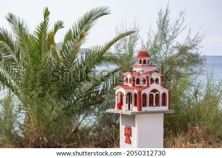 Traditional and memorial small chapel or church in Greece with palm tree and sea in background