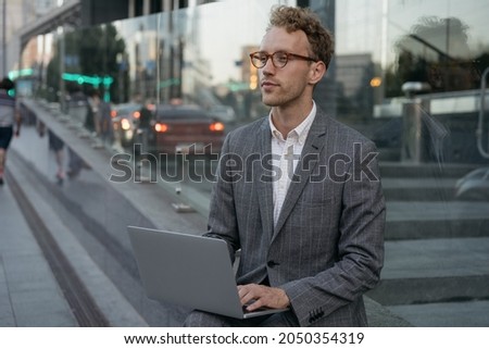 Portrait of pensive freelancer copywriter using laptop computer, typing, working online sitting on urban street