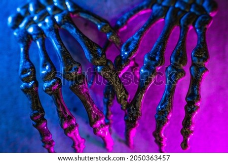 Pair of scary skull hands on texture background with blue and pink colored lights for halloween.