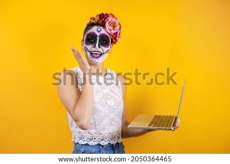 Mexican Catrina, portrait of young latin woman holding computer or laptop,  Halloween party in Mexico
