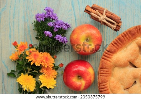 Mixed colorful mum flowers. Along side  apple pie and whole apples. Also a bundle of cinnamon sticks tied with twine. On a rustic green wooden background. 