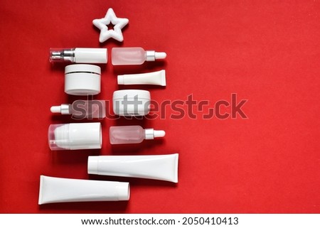 Creative composition. Moisturizer cream jars and serum bottles and white tubes in a Christmas tree shape on a red background. Skin care cosmetic products. Copy space.