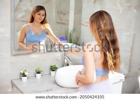 Beautiful pregnant brunette woman in the bathroom in front of the mirror. Hygiene. Self-care during pregnancy. Good morning. High quality photo