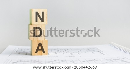Wooden block with words NDA - acronim - NON-DISCLOSURE AGREEMENT. NDA wooden blocks are on the paper gray background. business concept. space for text in right. front view.