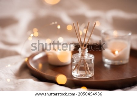 Home perfume in glass bottle with wood sticks, scented burn candles on tray in bedroom close up over white. Aromatherapy cozy atmosphere lifestyle. Winter warm xmas season. Good morning.  Royalty-Free Stock Photo #2050454936