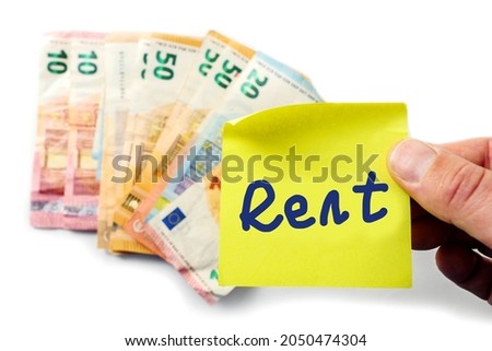 Yellow sticker with blue hand written sign rent over a pile of Euro bank notes. White isolated background. Paying household bills concept.