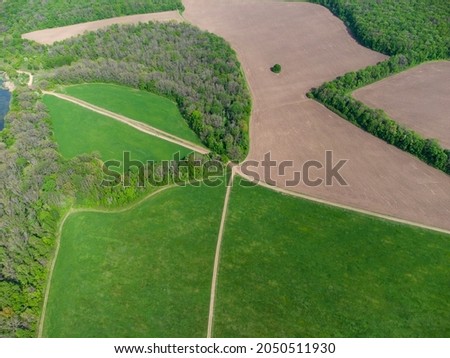 Aerial countryside on sunny day. Green summer rural landscape with pasture, dirt fields, road lines and forest around
