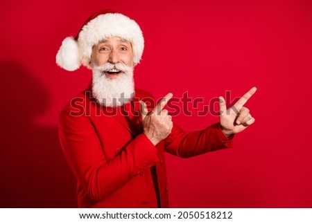Photo of charming cute mature man dressed christmas costume hat pointing fingers empty space isolated red color background