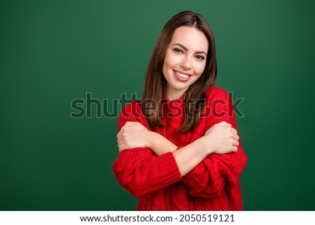 Photo portrait girl in red pullover embracing herself smiling isolated green color background copyspace