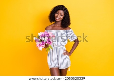 Photo of adorable positive dark skin person put hand on waist hold flowers isolated on yellow color background
