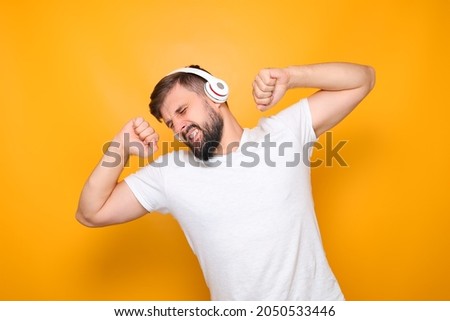 a bearded man in a white T-shirt and with headphones on his ears dances to the rhythm of the music.