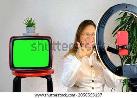 woman 40-45 years old, pretty female blogger sits in front of ring light and red smartphone, emotionally talks on topic of business, hobby during quarantine covid 19, old TV with green screen