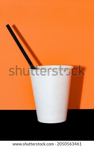 Eco-friendly white glass with a black straw on orange background. Halloween party concept. Copy space, free text, minimalism, monochrome, vintage