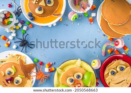 Creative homemade Halloween pancakes for breakfast, in form of funny monsters, ghost, bat, witch. With traditional trick or treat sweets, candy and decorations, top view on colorful blue background