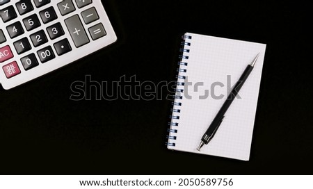 Large silver calculator with pen and white paper notebook on a black background. Copy space. Conceptual photo of calculations, accounting, computing, profit, loss, tax. Business card. Design mockup.