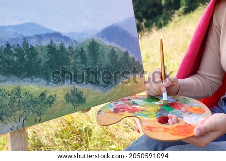 Young woman drawing on easel with brush outdoors, closeup