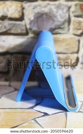 Photo of a blue plastic cell phone holder with a stone wall as a background on a stone motif table