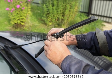 White working men's hands change the car wiper blade on the background of green grass at summer day, self seasonal car maintenance service Royalty-Free Stock Photo #2050598567