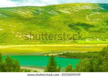 Turquoise meltwater flows in a river through mountains and forests landscape of Norway.