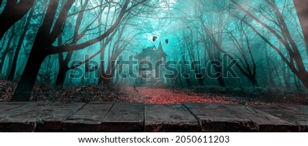 Halloween background. Rustic wooden board table in front of foggy autumn forest and witch's house. layout  for design cards, posters, invitations Royalty-Free Stock Photo #2050611203