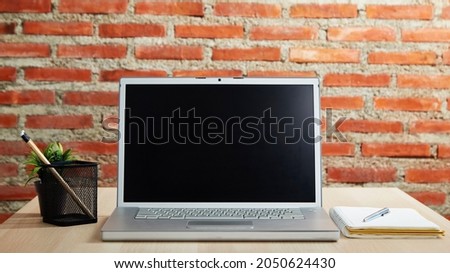 Laptop with blank screen on the desk and red brick wall work from home or study online