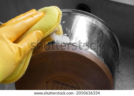 Person, wearing rubber gloves, cleaning a stainless steel and copper saucepan with a wadhing up foam pad Royalty-Free Stock Photo #2050636334