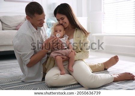 Happy couple holding their cute little baby with pacifier at home
