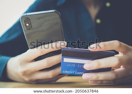 Selective focus on credit card was held by young woman's hand in blue casual, hold smart phone to buy product from the website on internet, e-commerce and online shopping as modern concept, e-payment