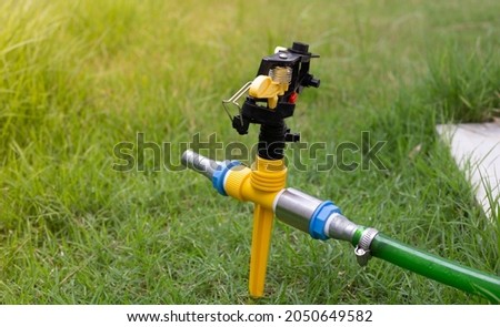 Yellow-black sprinkler for watering plants close-up on the green garden background of greenery.