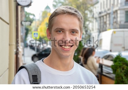 Street portrait of a smiling young guy 20-25 years old with a backpack on his shoulder against the background of old urban architecture. Perhaps he is an IT specialist or a tourist, a student 1. Royalty-Free Stock Photo #2050653254