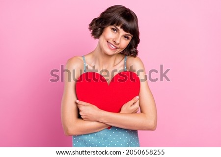 Portrait of attractive cheerful kind girl hugging holding heart shape form isolated over pink pastel color background