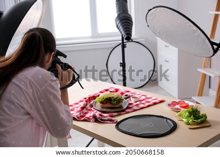 Young woman with professional camera taking photo of sandwich in studio. Food photography Royalty-Free Stock Photo #2050668158