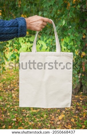 Stylish man hand holding white blank canvas tote shopping bag outdoor 