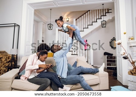 African american mother watching cartoons with daughter on digital tablet while father playing with another daughter. Happy parents enjoying time with their kids.