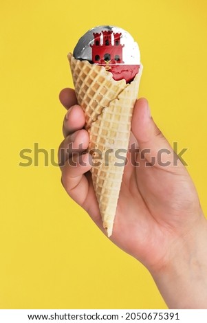 On a colorful background, a hand with ice cream in the form of the flag of Gibraltar