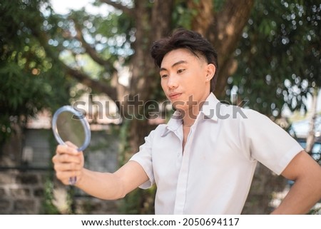 A vain young man checks his looks in the mirror. Narcissistic behavior. Outdoor scene. Royalty-Free Stock Photo #2050694117