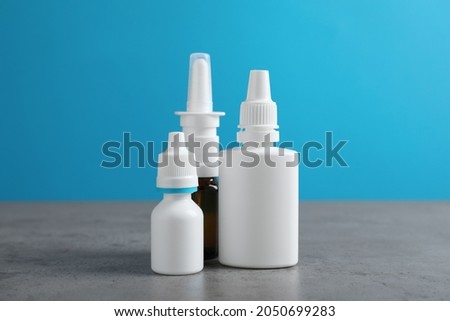 Nasal sprays in different bottles on grey table against light blue background