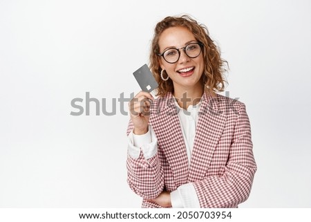 Confident business woman showing credit card and smiling, standing in suit and glasses against white background