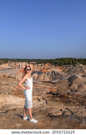 A young girl in a white dress in the middle of a clay quarry.A beautiful woman on the background of a beautiful landscape.Top view of the hills made of refractory clay.Girl in sunglasses 