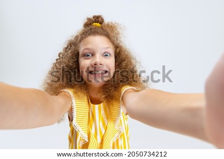 Selfie. Front camera view of little smiling curly beautiful girl looking at camera isolated over white studio background. Childhood, play, family, fun, action concept. Copyspace for ad.
