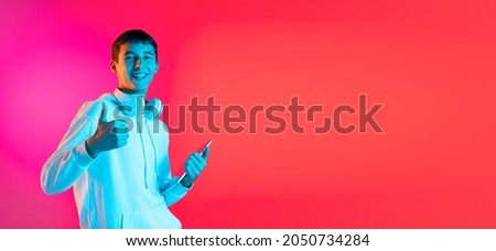 Thumbs up, nice sign. Portrait of young man, student or boy in casual clothes smiling isolated on magenta studio backgroud in neon. Human emotions, facial expression, youth fashion concept. Flyer