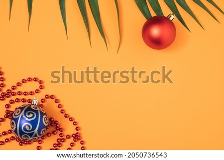 Christmas composition of Christmas tree toys and red beads on an orange background and palm branches. Minimal flat lay.