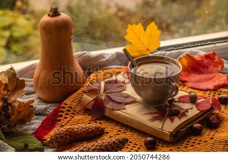 Autumn still life with a cup of tea with lemon on the windowsill among the autumn leaves and tall pumpkin.