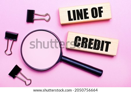 On a pink background, a magnifier, black paper clips and wooden blocks with the text LINE OF CREDIT. Business concept