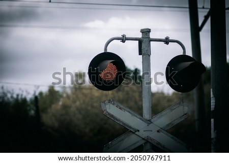 A red flashing traffic light and a road sign at a railway crossing