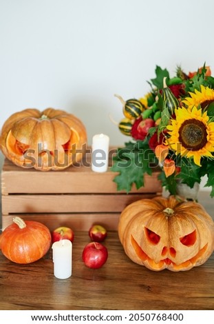 Autumn holiday concept: pumpkins, candles, sunflower and other attributes at the table as Halloween party theme background. Halloween orange pumpkin with evil scary faces. High quality vertical photo