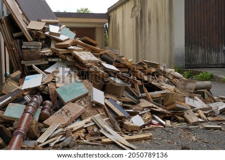 Dismantled furniture on a yard between two buildings. There are pieces of wooden furniture piled up. They are of irregular size. It looks like vacating of a dwelling.