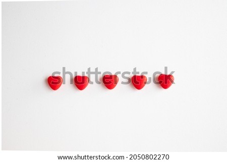 Group of red heart shaped candies placed side by side on white background, isolated red hearts, top view
