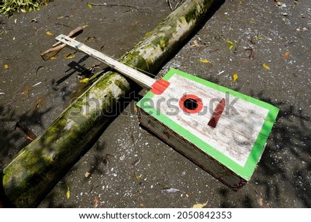 Homemade bass guitar set on logs and sand. This guitar model was made by rural residents to accompany the song with soft wood material and nylon rope                           Royalty-Free Stock Photo #2050842353